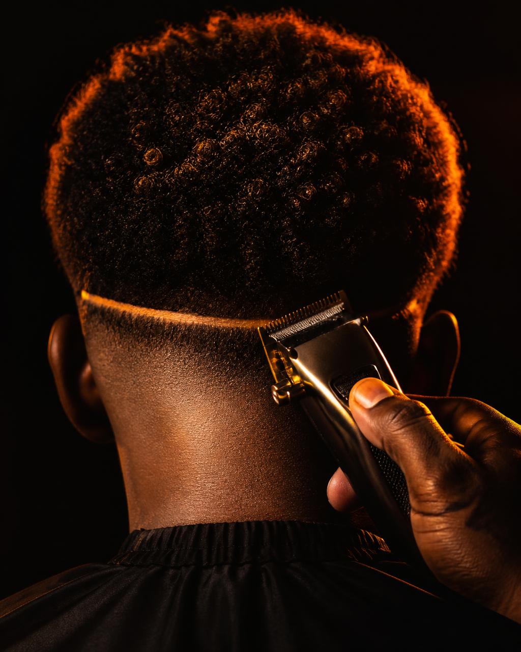 Clippers carving a razor-sharp skin fade on coily hair, seen from behind