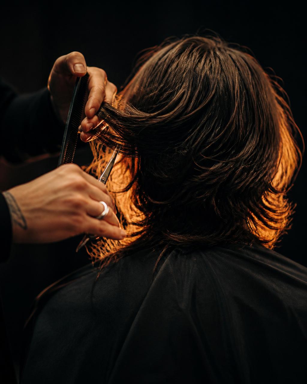 Scissors cutting shoulder-length hair from behind, strands glowing in orange back light